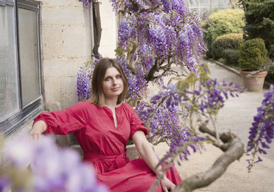 Young woman in red dress sits on a bench in the thickets of blooming wisteria