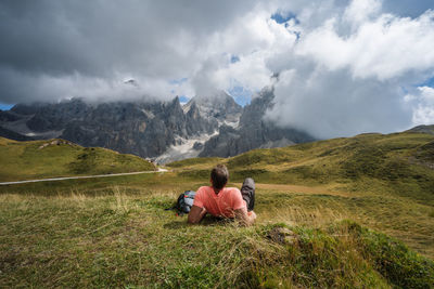 Rear view of man sitting on mountain against sky