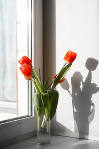Bouquet of red tulips in a vase standing on the windowsill by the window. vertical photo
