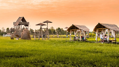 People on field by houses against sky during sunset