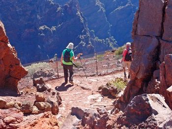 Rear view of men walking on rocks against mountains