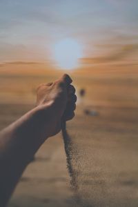 Cropped image of hand pouring sand during sunset