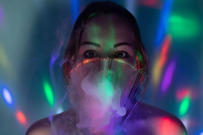 Close-up portrait of young woman holding illuminated fiber optic in darkroom