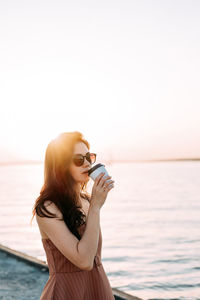 Young woman standing against sea against clear sky