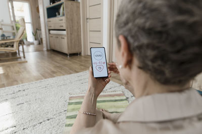 Mature woman checking data on smartphone at home