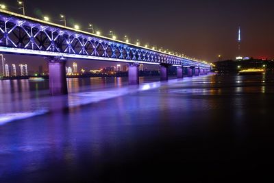 Illuminated bridge over river in city at night