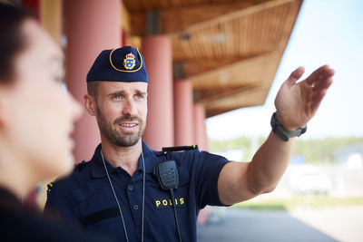 Male police officer gesturing while directing coworker outside police station
