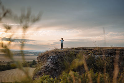 Rear view of man walking on field against sky during sunset