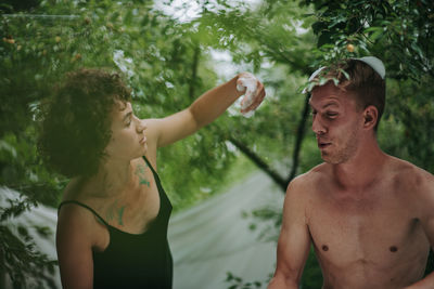 Midsection of shirtless man and woman standing against trees