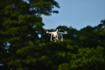 Low angle view of quadcopter flying by trees against clear sky