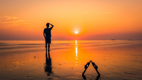 Silhouette man standing at beach against orange sky during sunset