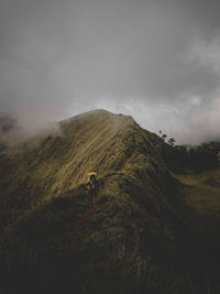 Rear view of man climbing on mountain ridge against sky