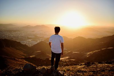 Rear view of man standing on rock at sunset