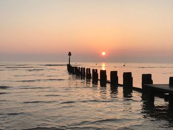 Silhouette wooden post on pier over sea against sky during sunset