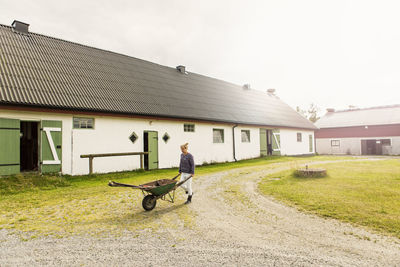 Female farmer pushing wheelbarrow on dirt road by barn