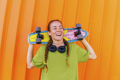 Portrait of smiling young man holding camera while standing against orange wall