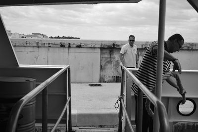 People standing on railing by sea against sky