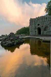 Old building by lake against sky during sunset