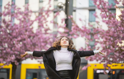 Woman with arms outstretched standing against building in city