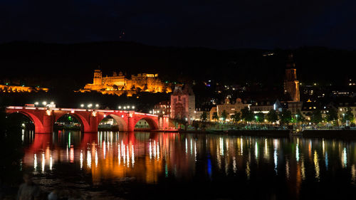Illuminated bridge over river by buildings against sky at night