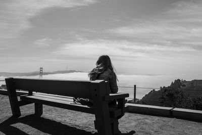 Rear view of woman sitting on bench looking at view