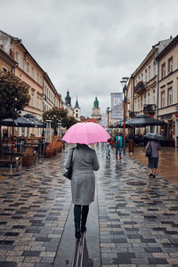 Back view of woman holding pink umbrella walking in a downtown on rainy gloomy autumn day