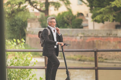 Side view full length young businessman in a suit riding an electric scooter while commuting to work 