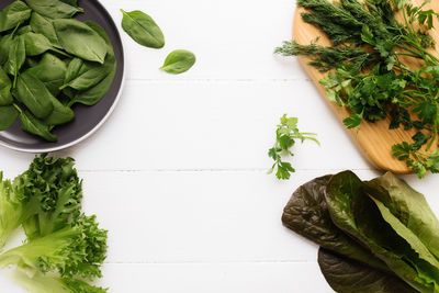 Cutting board, bowl of fresh green salad leaves, romaine and parsley, basil on white background