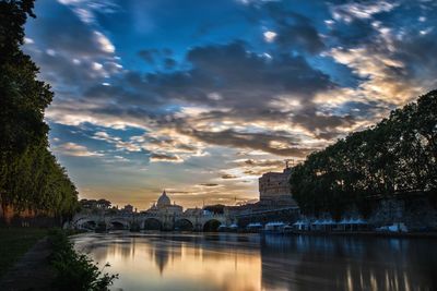 Scenic view of river by buildings against sky during sunset