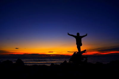 Silhouette man standing on rock at beach against sky during sunset