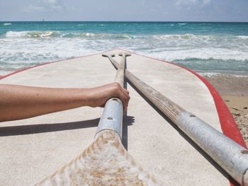 Cropped hand holding oar at beach on sunny day