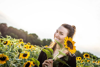 Young woman in sunflower field against sky