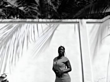 Rear view of woman standing against white wall under palm tree shade