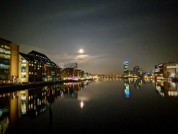 Illuminated buildings by river against sky at night