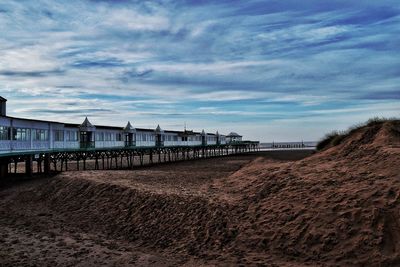 Stilt houses at beach against cloudy blue sky