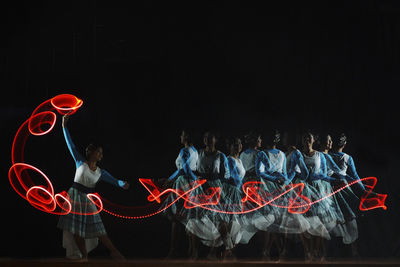 Multiple image of woman making light painting against black background