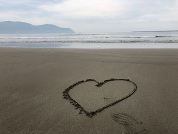 Heart shape on sand at beach against sky