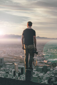 Full length of man with camera standing against cityscape during sunny day