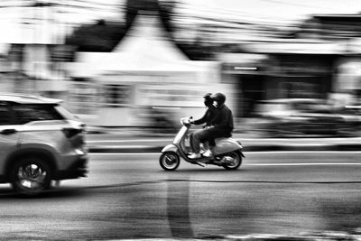 Blurred motion of man riding motor scooter on street