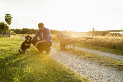 Man with dog in grassy field at farm against sky