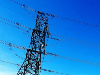 Low angle view of electricity pylon against clear blue sky