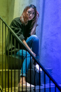 Portrait of young woman sitting on staircase against wall
