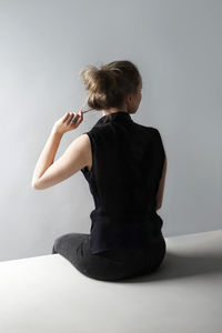 Rear view of woman sitting against white background