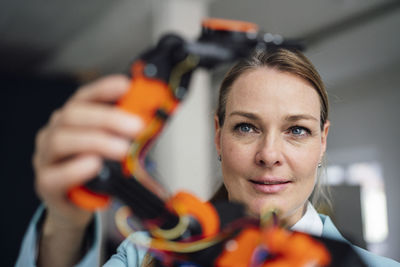 Smiling engineer examining robotic arm at office