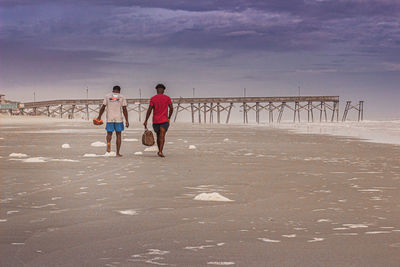 Rear view of people walking on beach against sky