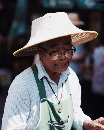 PORTRAIT OF MAN WITH HAT STANDING AGAINST BLURRED BACKGROUND