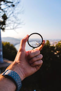 Close-up of hand holding magnifying glass against sky