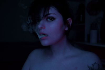 Portrait of a young woman in neon light exhaling smoke