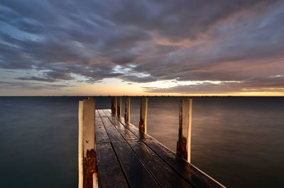 Wooden pier over sea against sky at sunset