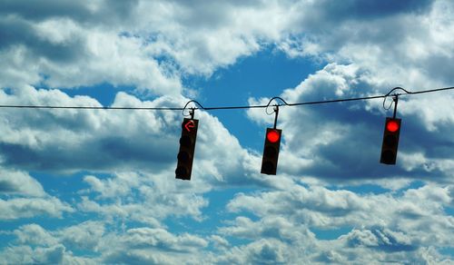 Low angle view of stoplights against cloudy sky